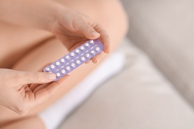 Photo of Woman with blister of contraceptive pills on sofa indoors, closeup. Space for text