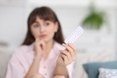 Woman with blister of contraceptive pills indoors, selective focus