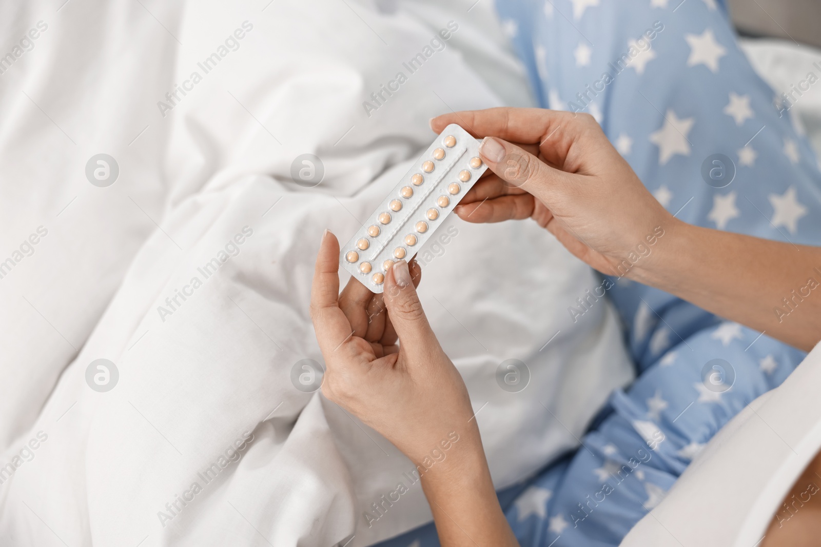 Photo of Woman with blister of contraceptive pills on bed, top view