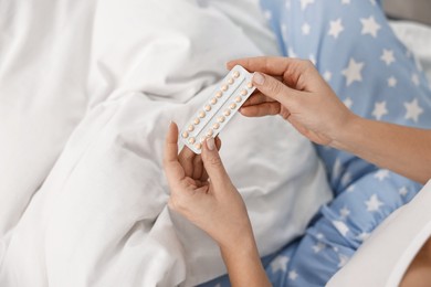 Photo of Woman with blister of contraceptive pills on bed, top view