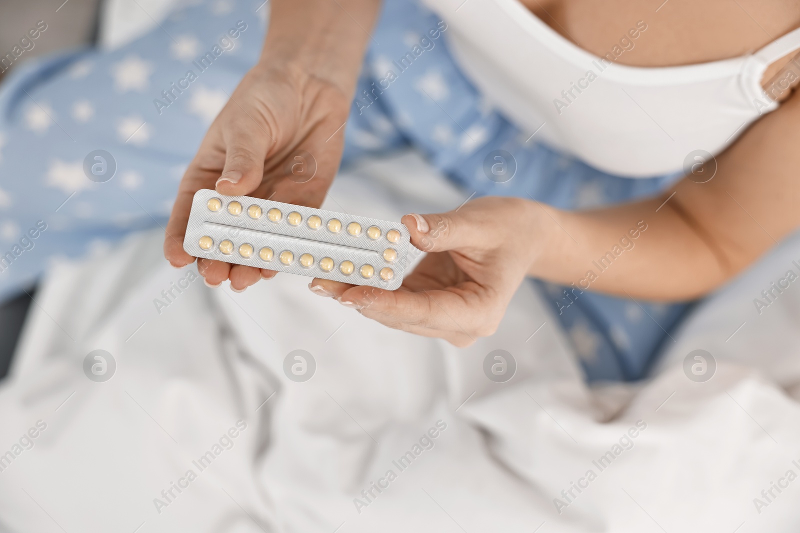 Photo of Woman with blister of contraceptive pills on bed, top view