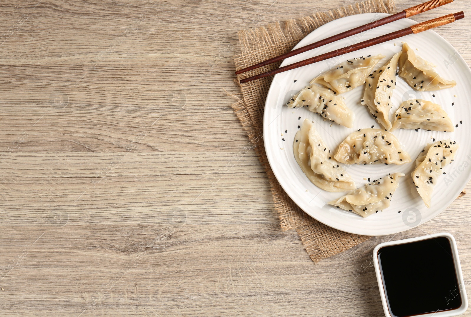 Photo of Delicious gyoza dumplings with sesame seeds served on wooden table, top view. Space for text