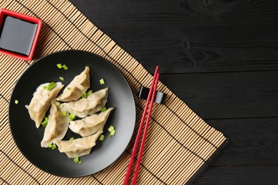 Photo of Delicious gyoza dumplings with chives served on black wooden table, top view. Space for text