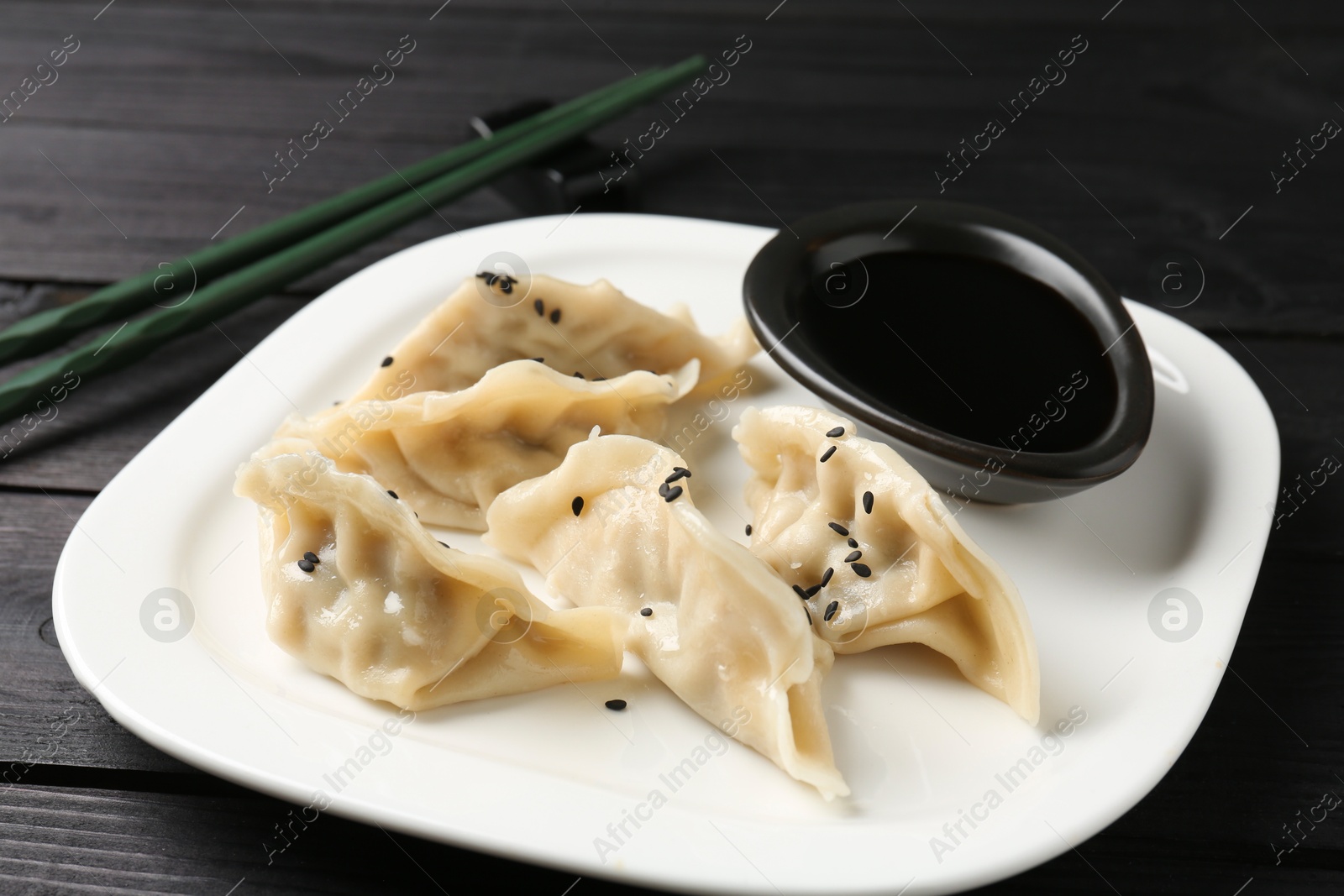 Photo of Delicious gyoza dumplings with sesame seeds served on black wooden table, closeup