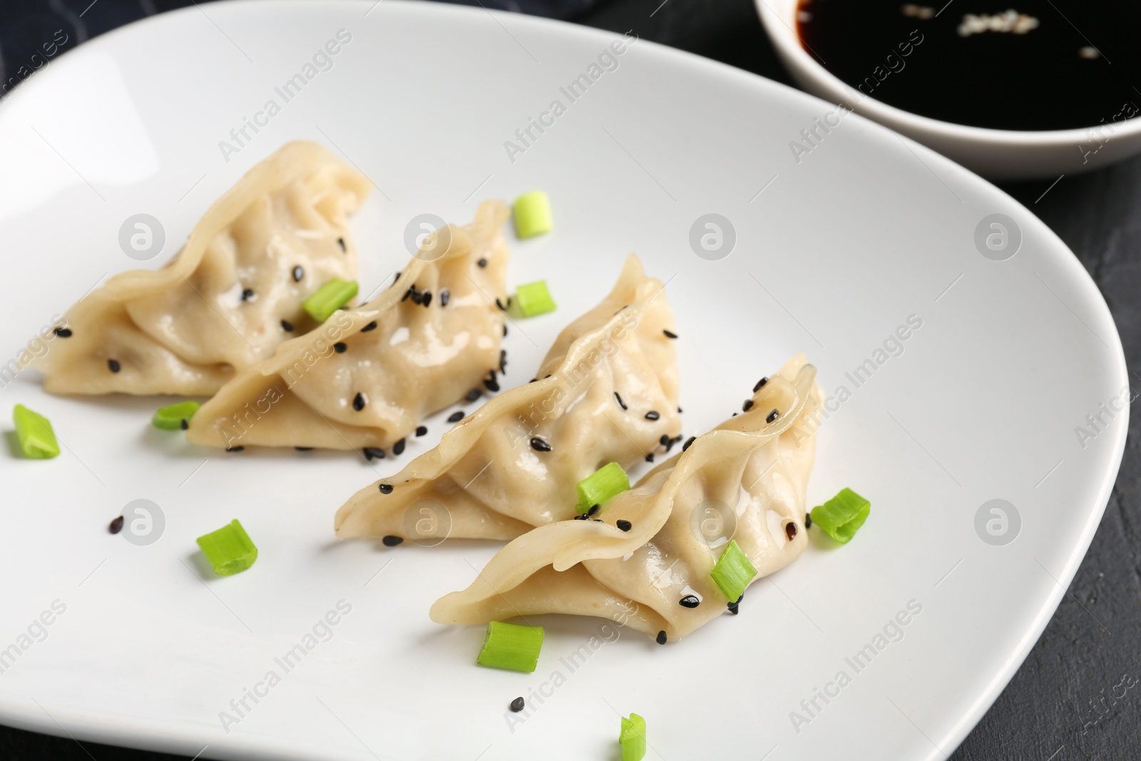 Photo of Delicious gyoza dumplings with chives and sesame seeds served on black table, closeup