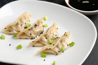 Photo of Delicious gyoza dumplings with chives and sesame seeds served on black table, closeup