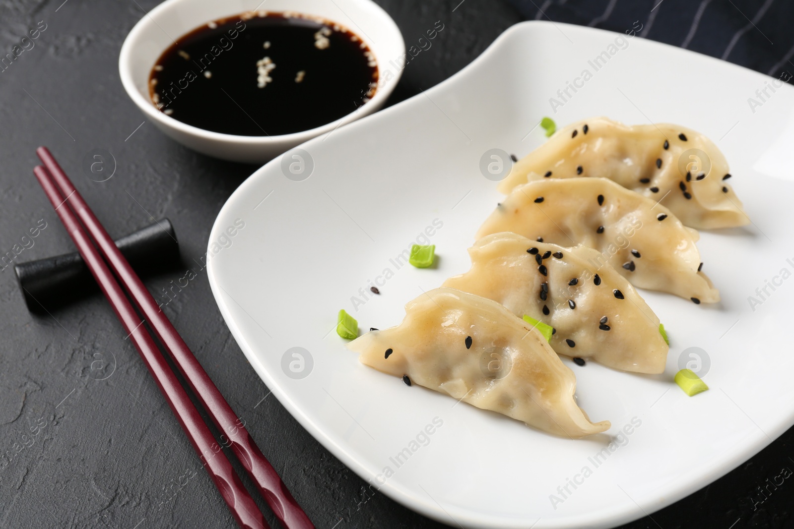 Photo of Delicious gyoza dumplings with chives and sesame seeds served on black table, closeup