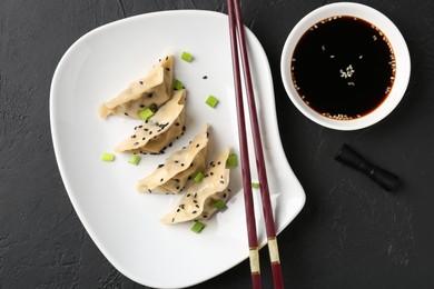 Photo of Delicious gyoza dumplings with chives and sesame seeds served on black table, top view