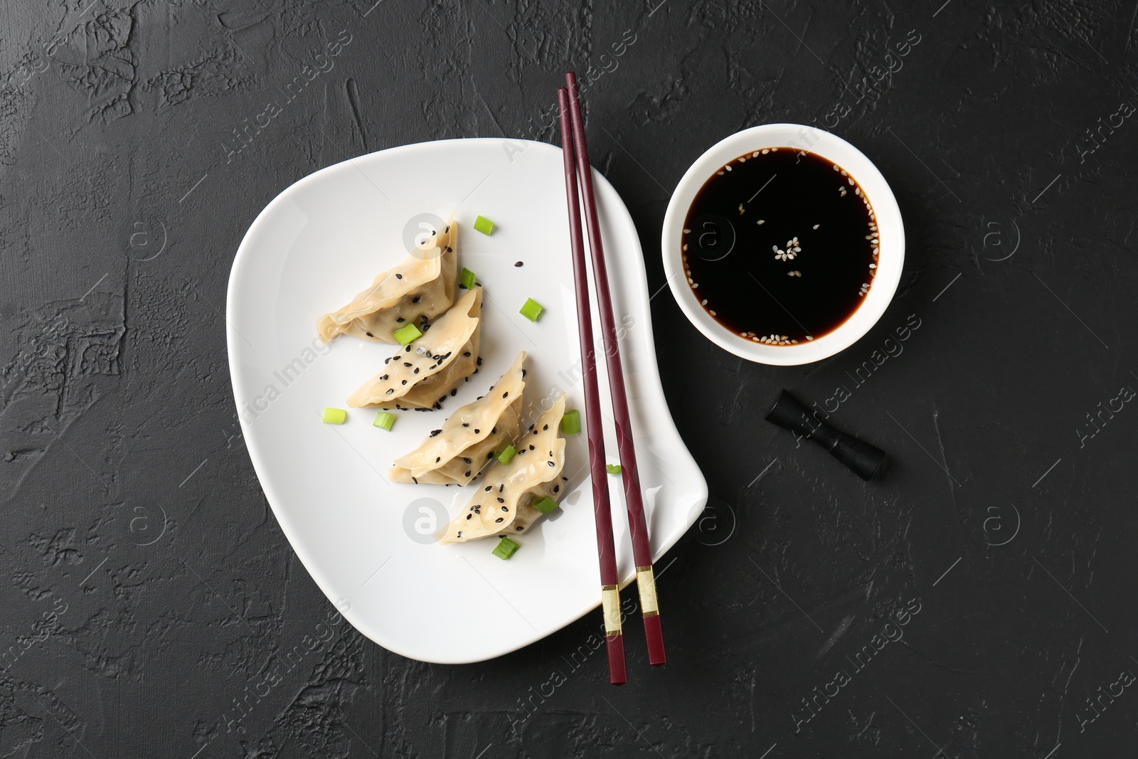 Photo of Delicious gyoza dumplings with chives and sesame seeds served on black table, top view