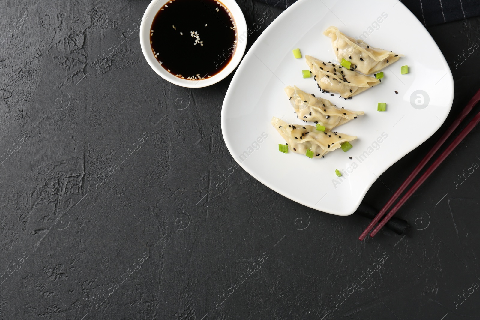 Photo of Delicious gyoza dumplings with chives and sesame seeds served on black table, top view. Space for text