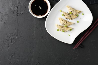 Photo of Delicious gyoza dumplings with chives and sesame seeds served on black table, top view. Space for text