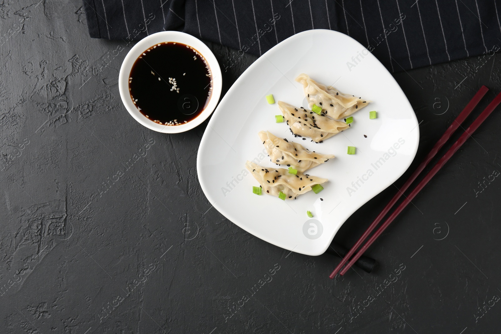 Photo of Delicious gyoza dumplings with chives and sesame seeds served on black table, top view. Space for text