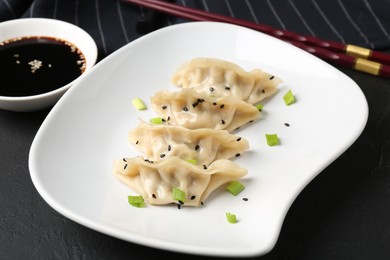 Photo of Delicious gyoza dumplings with chives and sesame seeds served on black table, closeup