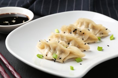 Photo of Delicious gyoza dumplings with chives and sesame seeds served on black table, closeup