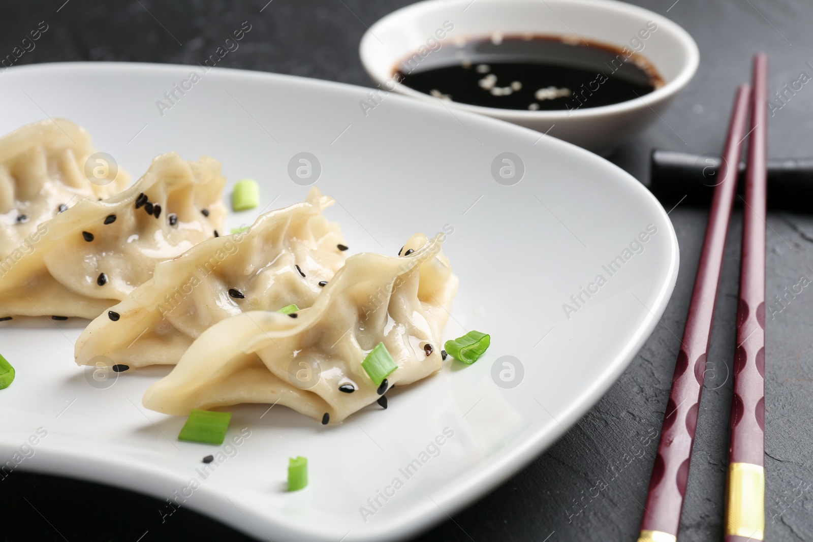 Photo of Delicious gyoza dumplings with chives and sesame seeds served on black table, closeup