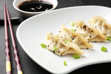 Photo of Delicious gyoza dumplings with chives and sesame seeds served on black table, closeup