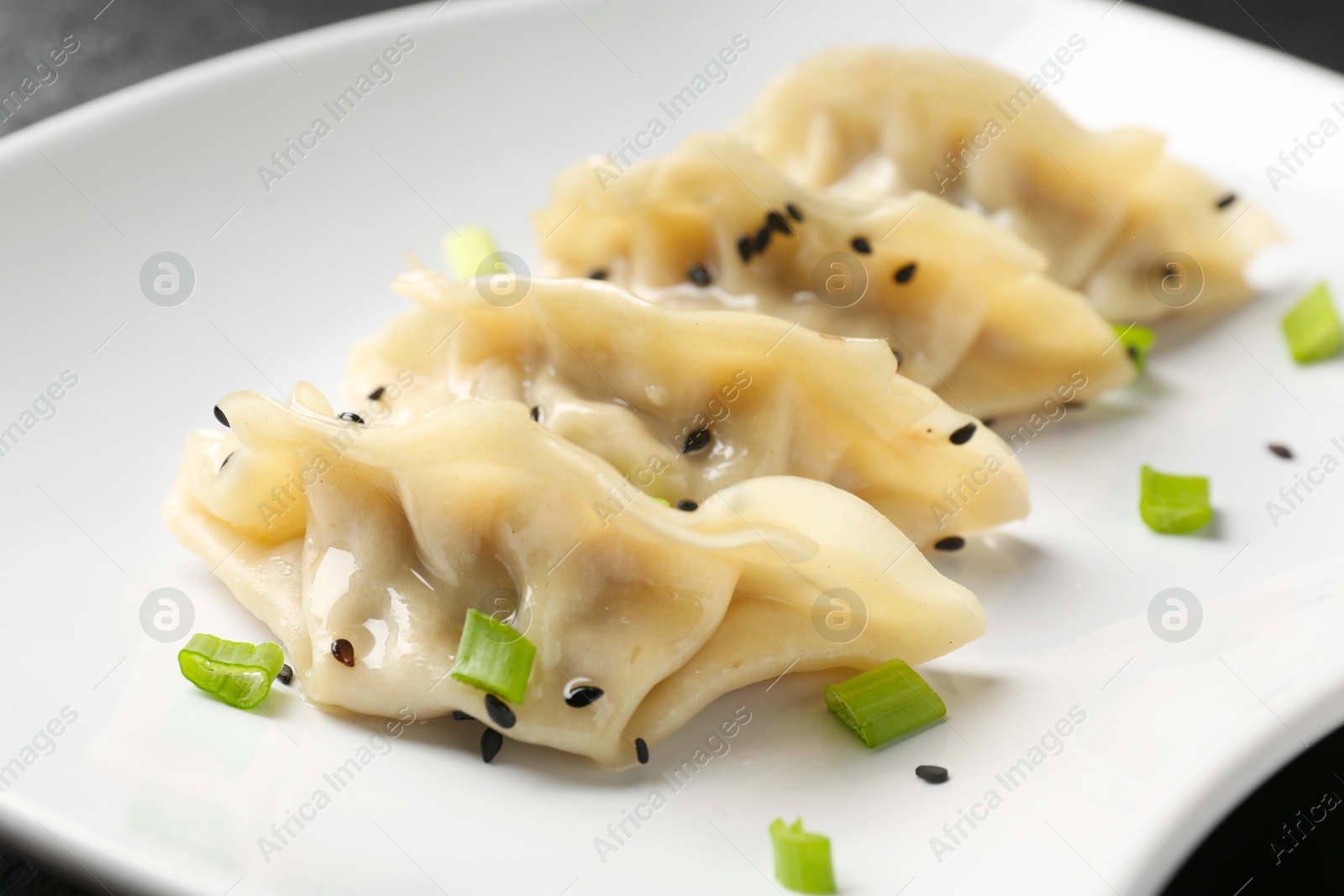 Photo of Delicious gyoza dumplings with chives and sesame seeds served on table, closeup