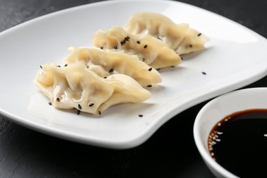 Photo of Delicious gyoza dumplings with sesame seeds served on black table, closeup