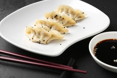 Photo of Delicious gyoza dumplings with sesame seeds served on black table, closeup