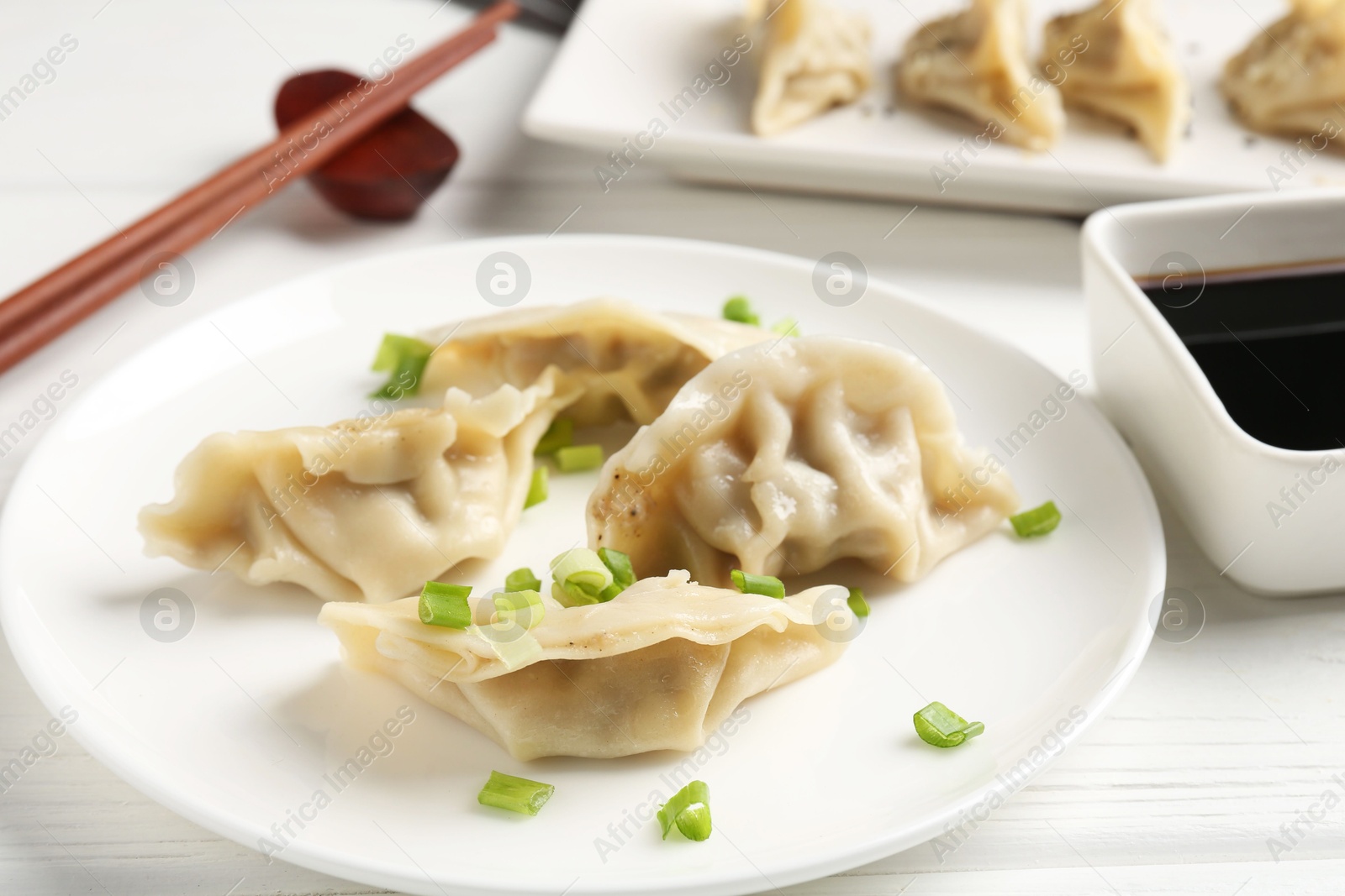 Photo of Delicious gyoza dumplings with chives served on white table, closeup