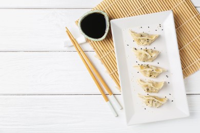 Photo of Delicious gyoza dumplings with sesame seeds served on white wooden table, top view. Space for text