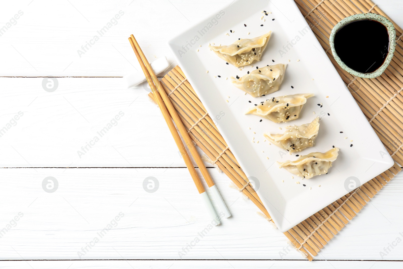 Photo of Delicious gyoza dumplings with sesame seeds served on white wooden table, top view. Space for text