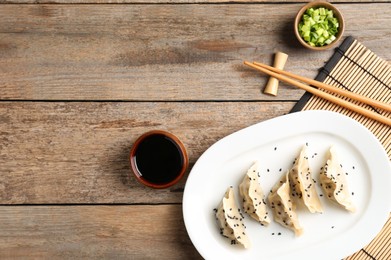 Photo of Delicious gyoza dumplings with sesame seeds served on wooden table, top view. Space for text