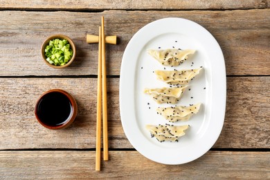 Photo of Delicious gyoza dumplings with sesame seeds served on wooden table, top view