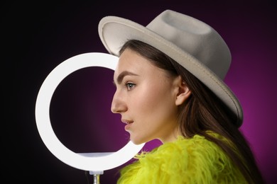 Photo of Stylish woman with ring lamp on dark purple background