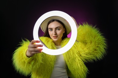 Photo of Stylish woman on dark purple background, view through ring lamp