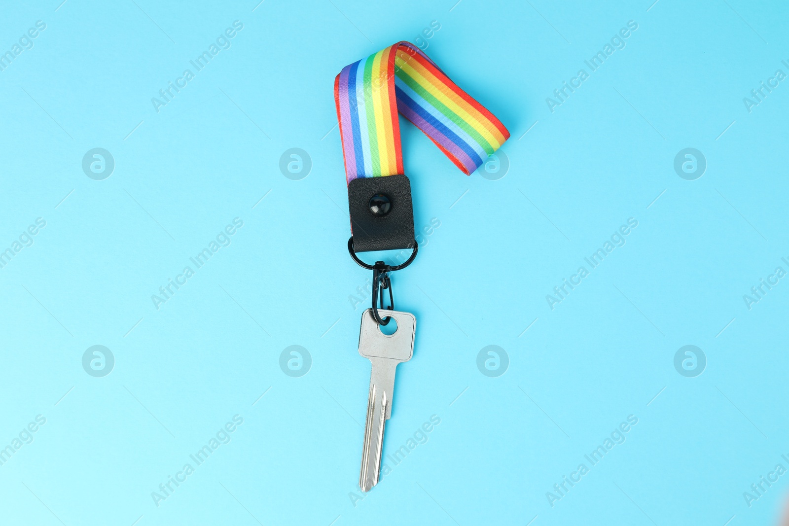 Photo of Key with keychain in LGBT colors on light blue background, top view