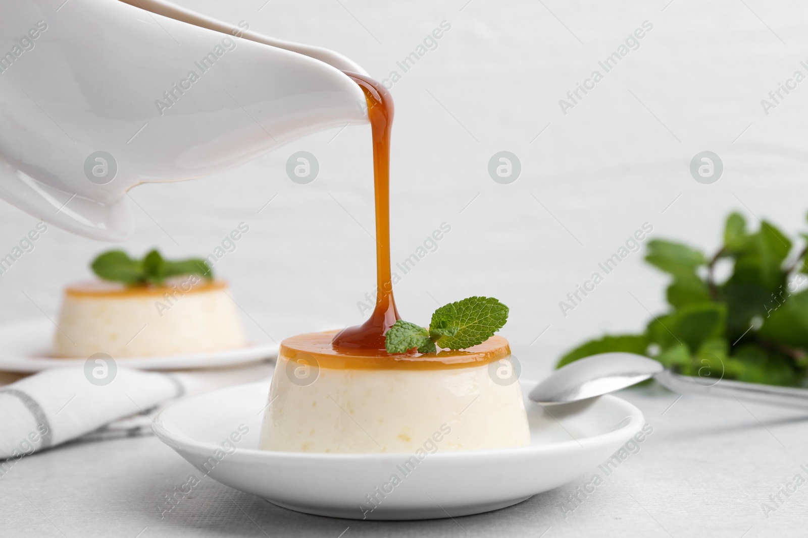 Photo of Pouring caramel sauce onto tasty pudding on white table, closeup