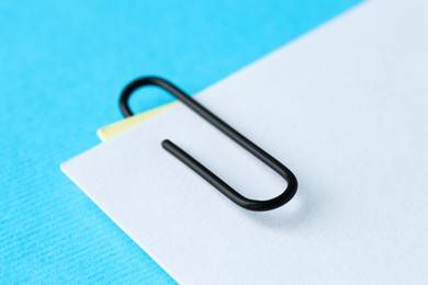 Photo of Paper notes with clip on light blue background, closeup