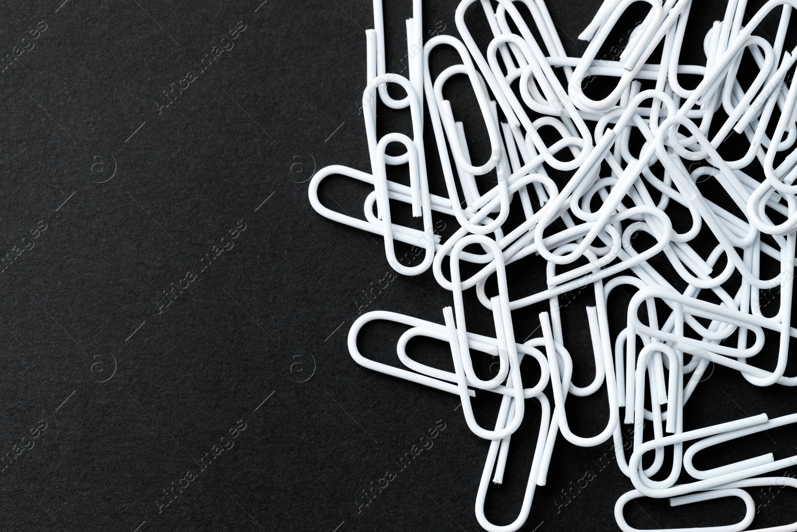 Photo of Many white paper clips on black table, top view. Space for text