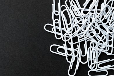 Many white paper clips on black table, top view. Space for text