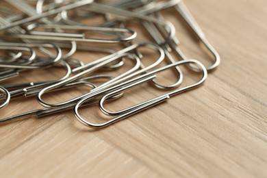 Photo of Many metal paper clips on wooden table, closeup. Space for text