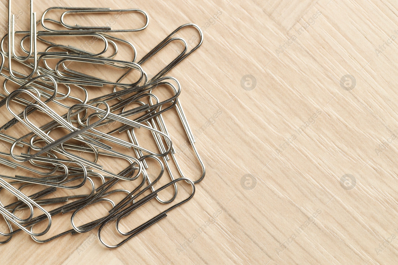 Photo of Many metal paper clips on wooden table, top view. Space for text