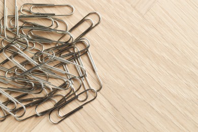 Photo of Many metal paper clips on wooden table, top view. Space for text