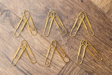 Many golden paper clips on wooden table, flat lay