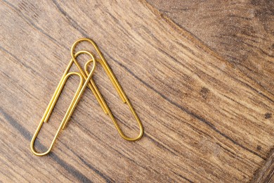 Two golden paper clips on wooden table, top view. Space for text