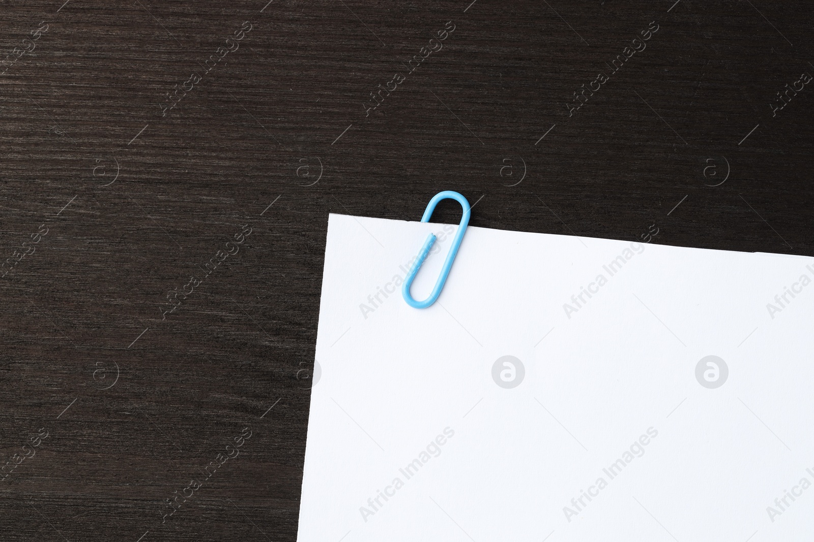 Photo of Paper note with clip on black wooden table, top view. Space for text