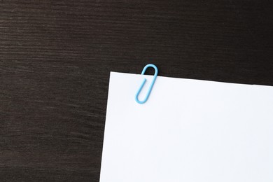 Photo of Paper note with clip on black wooden table, top view. Space for text