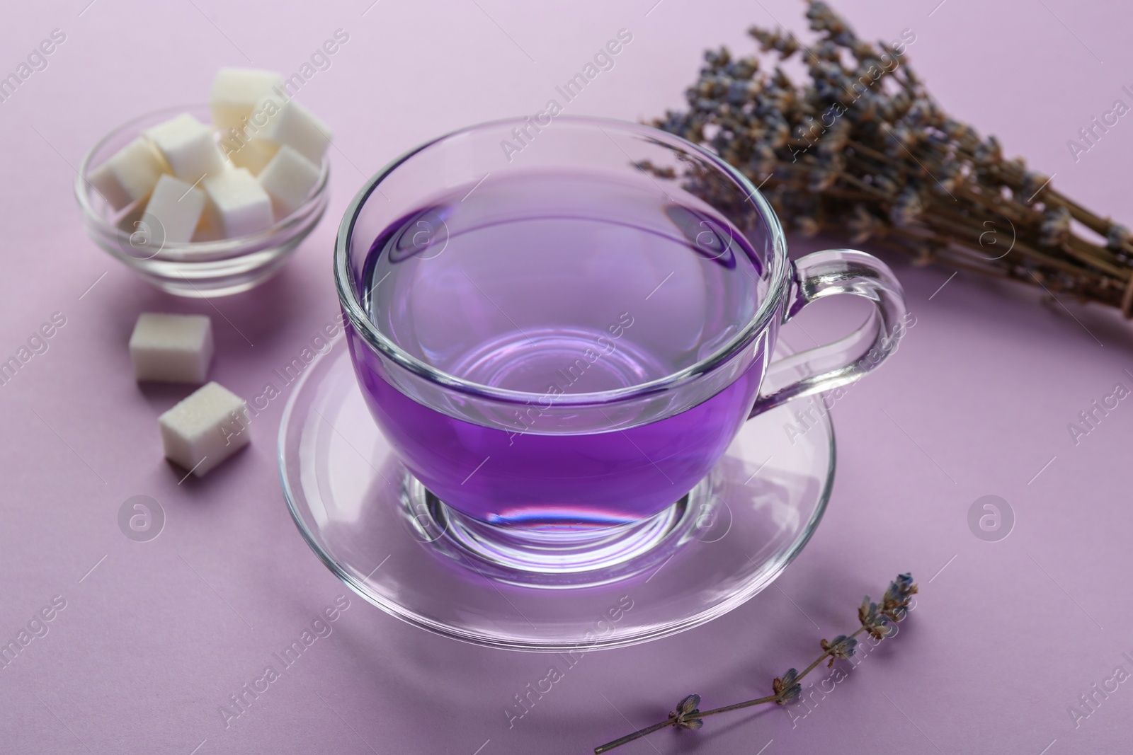 Aromatic lavender tea in glass cup, sugar cubes and dry flowers on lilac background, closeup Photo of Aromatic lavender tea in glass cup, sugar cubes and dry flowers on lilac background, closeup