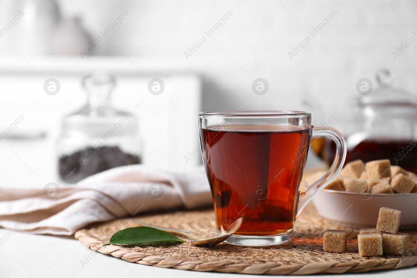 Photo of Aromatic black tea in cup and brown sugar cubes on white table, closeup