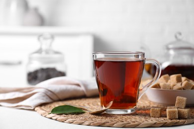 Photo of Aromatic black tea in cup and brown sugar cubes on white table, closeup