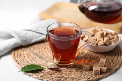 Photo of Aromatic black tea in cup and brown sugar cubes on white table, closeup