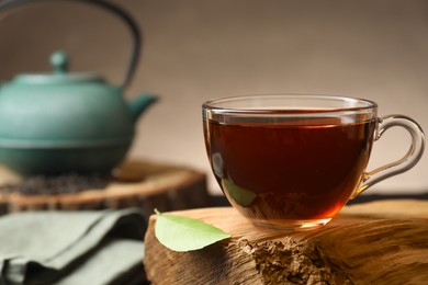 Aromatic black tea in cup and green leaf on wooden snag, closeup