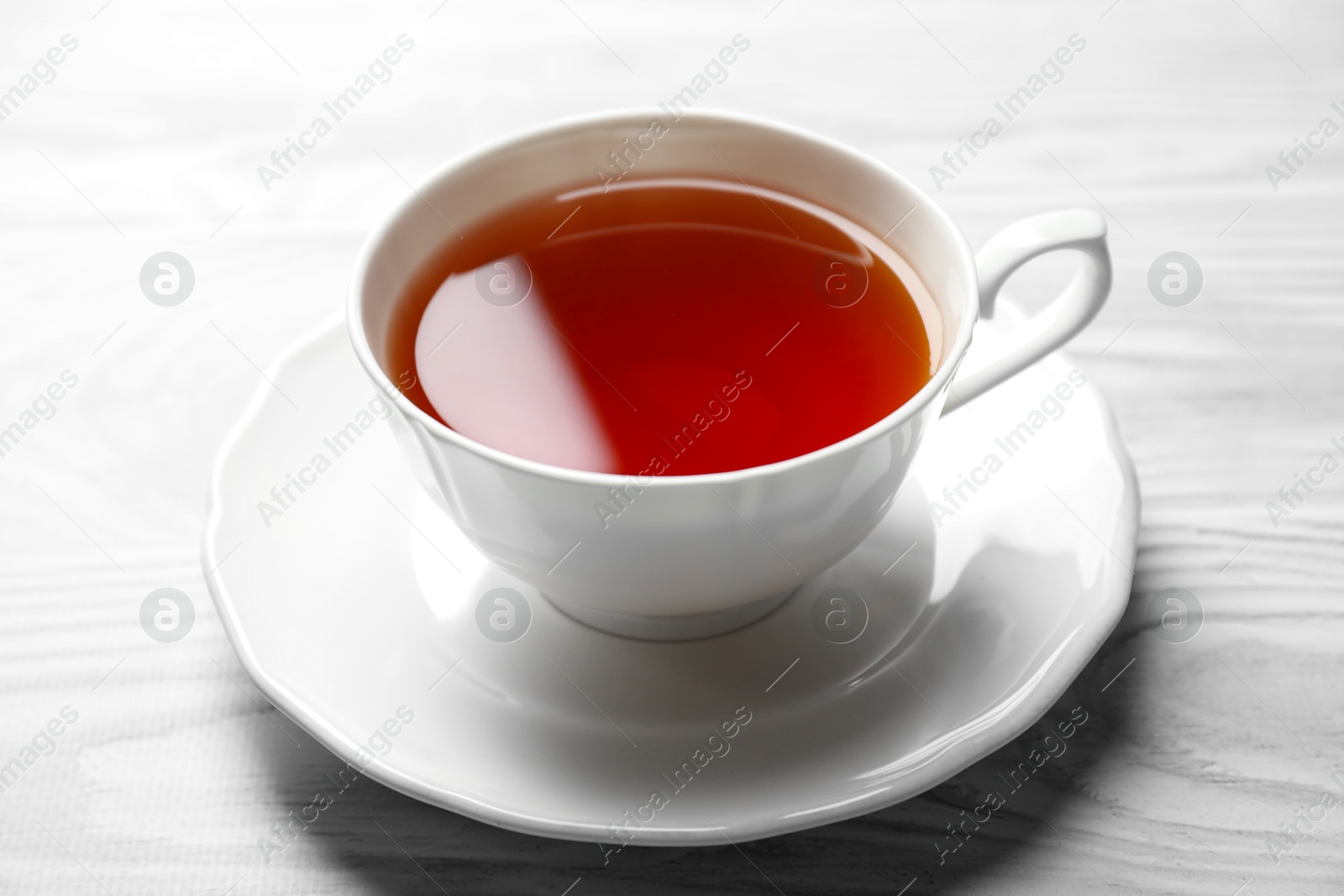 Photo of Aromatic black tea in cup on light blue wooden table, closeup