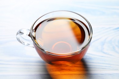 Aromatic black tea in cup on light blue wooden table, closeup