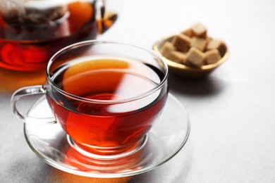 Photo of Aromatic black tea in cup and sugar on light table, closeup